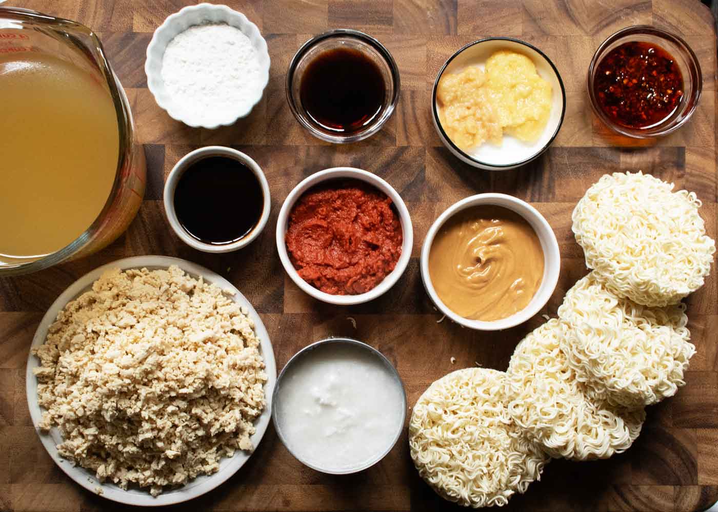 Ingredients for Spicy Peanut Chili Crisp Ramen Noodle Soup measured out into separate containers, arranged on a wooden board.